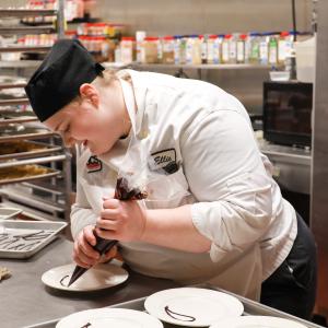 Culinary student working in kitchen piping dessert