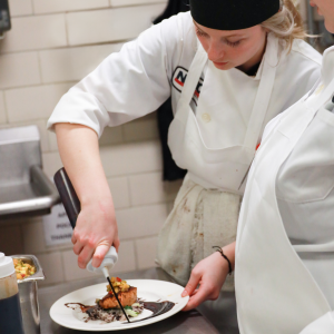 Culinary student working in kitchen plating food