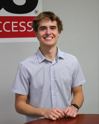 student with button-up shirt standing next to a table