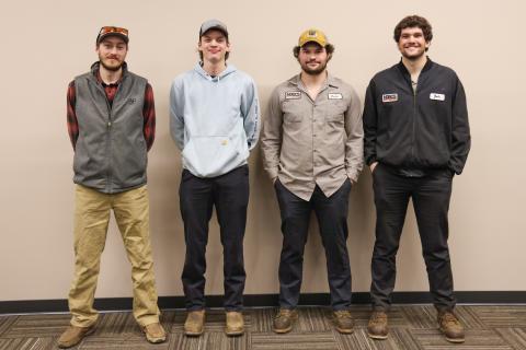 4 students standing side by side against a blank wall